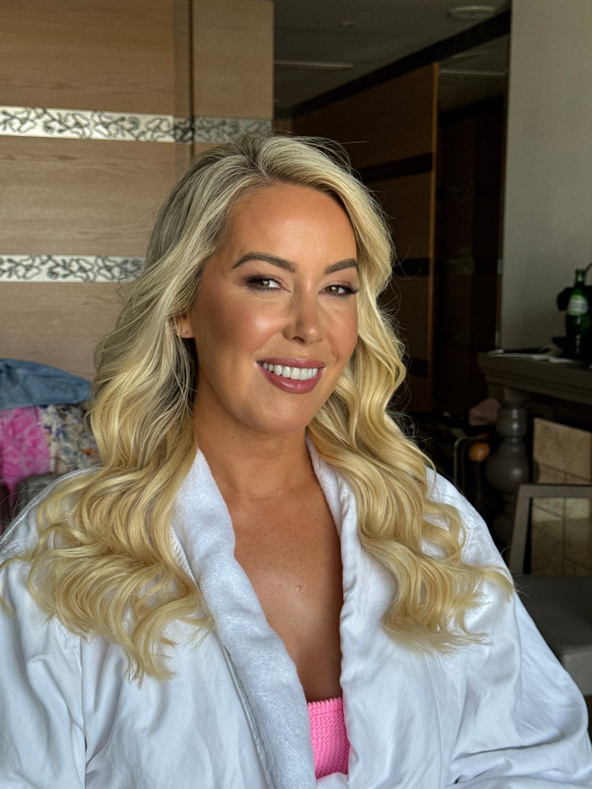 Bride with long blonde waves and warm, glowing makeup, photographed in her robe before she dresses