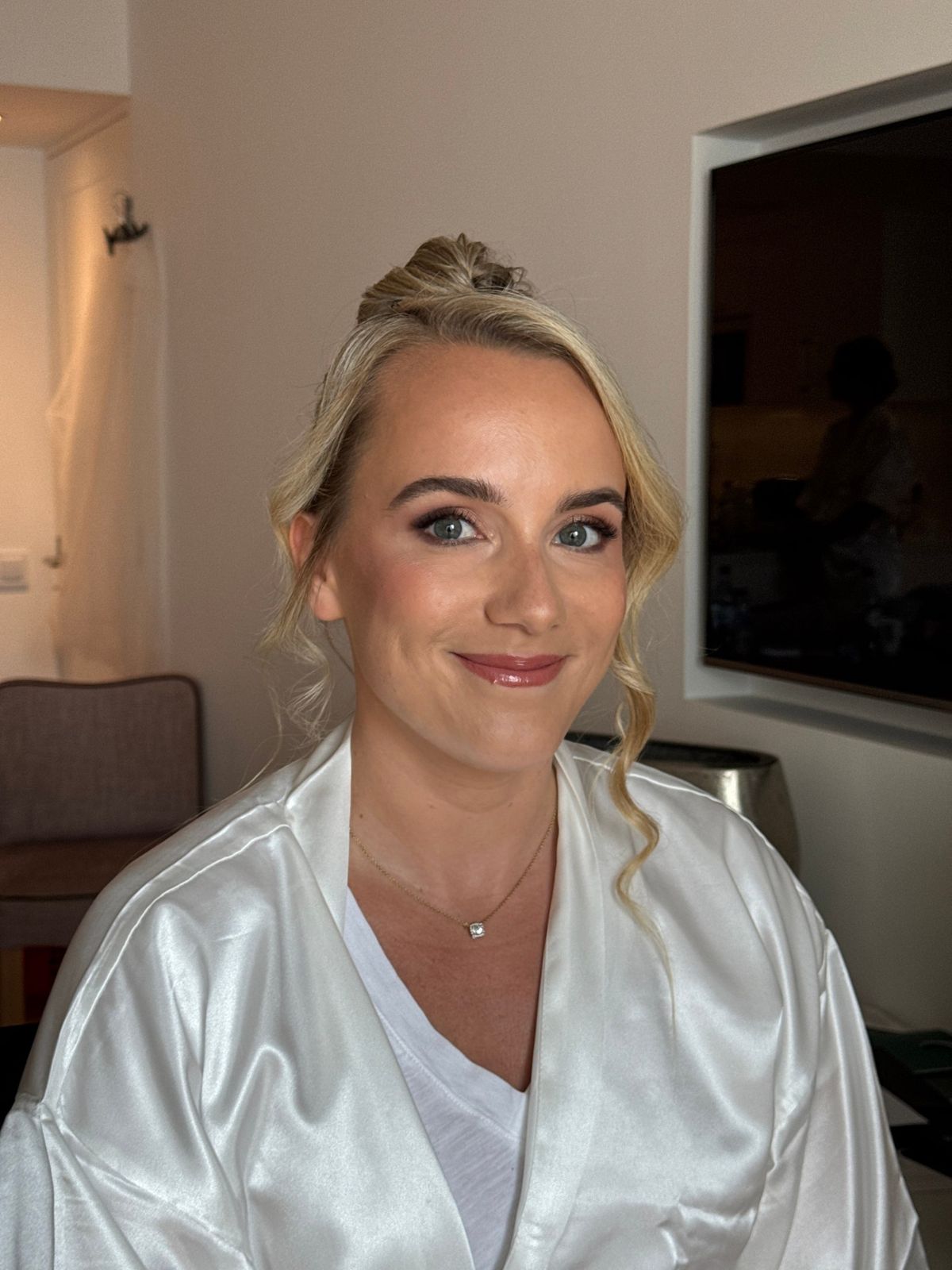 Bride with a soft twisted updo and luminous skin, photographed in her robe on the wedding morning