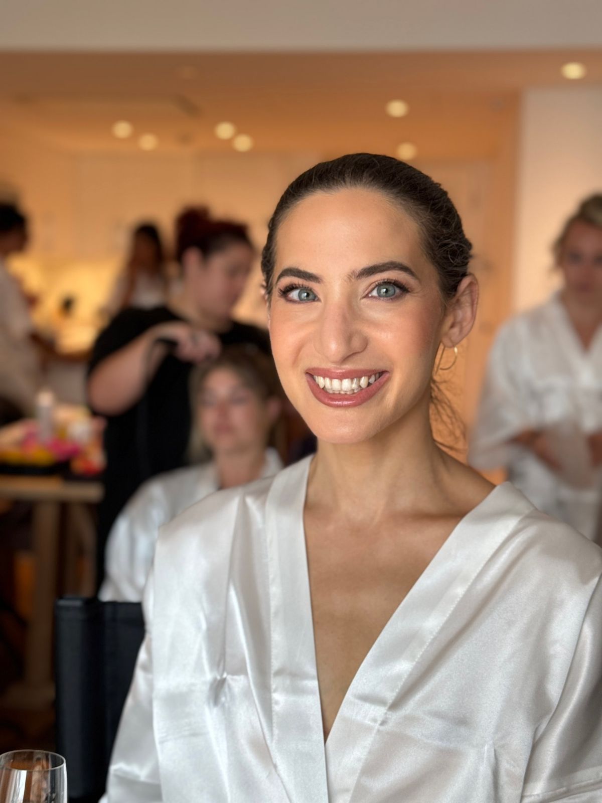 Bride with her hair in a low bun and softly defined eyes, the room getting ready behind her