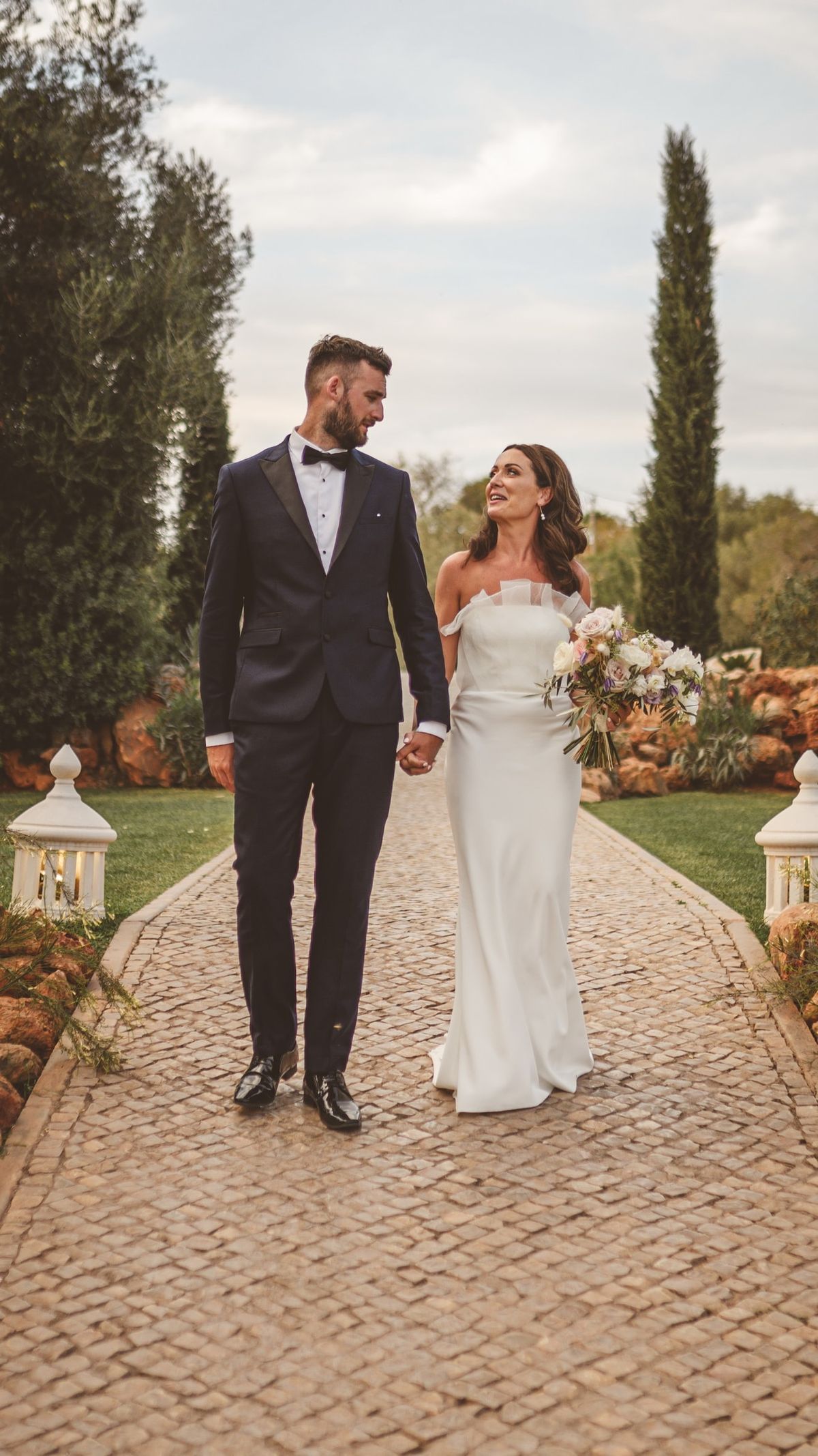 Bride and groom holding hands as they walk a cobbled garden path at their wedding venue