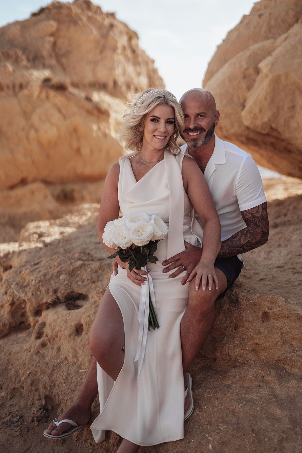 Bride and groom on the golden cliffs of the Algarve, the bride holding a bouquet of white roses
