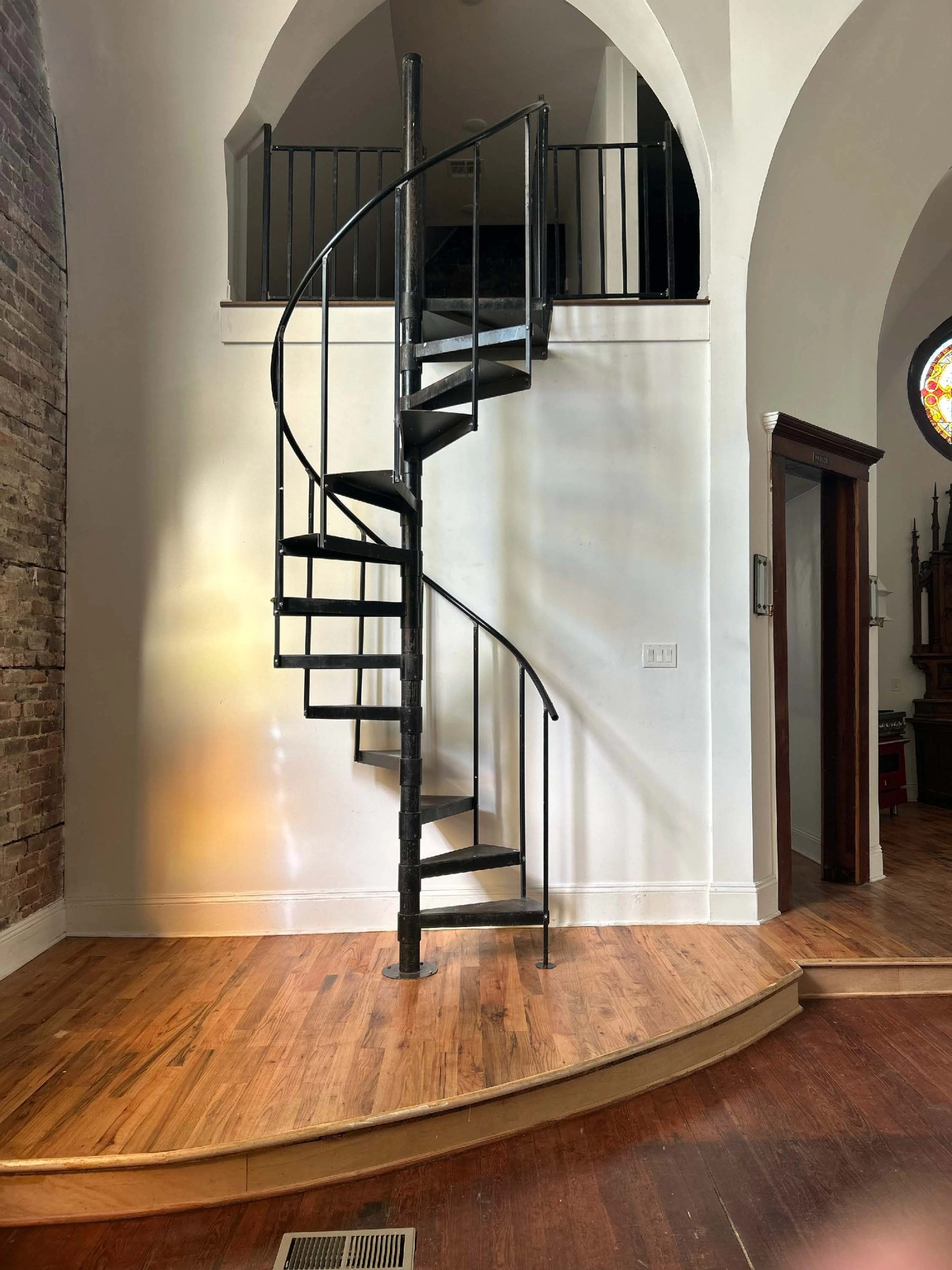 Spiral staircase rising from a wood floor beside an arched opening