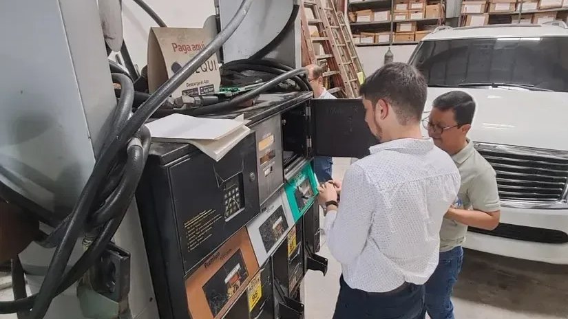 Two technicians inspect the interior of a fuel dispenser in a workshop.