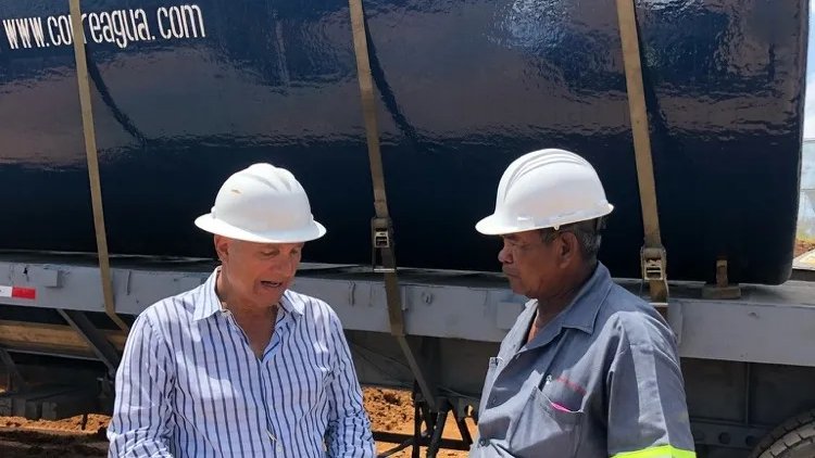 Dos trabajadores con casco conversan junto a un tanque de combustible instalado sobre un remolque.