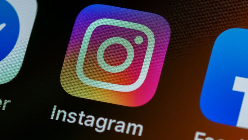 The image depicts a close-up view of a smartphone screen featuring the application icons for Instagram and Facebook. The Instagram icon is prominently displayed, showcasing its signature camera logo against a gradient background.