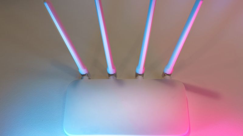 The image features a modern wireless router with four antennas, illuminated by colorful blue and pink lighting. The minimalist design emphasizes a sleek and contemporary aesthetic.