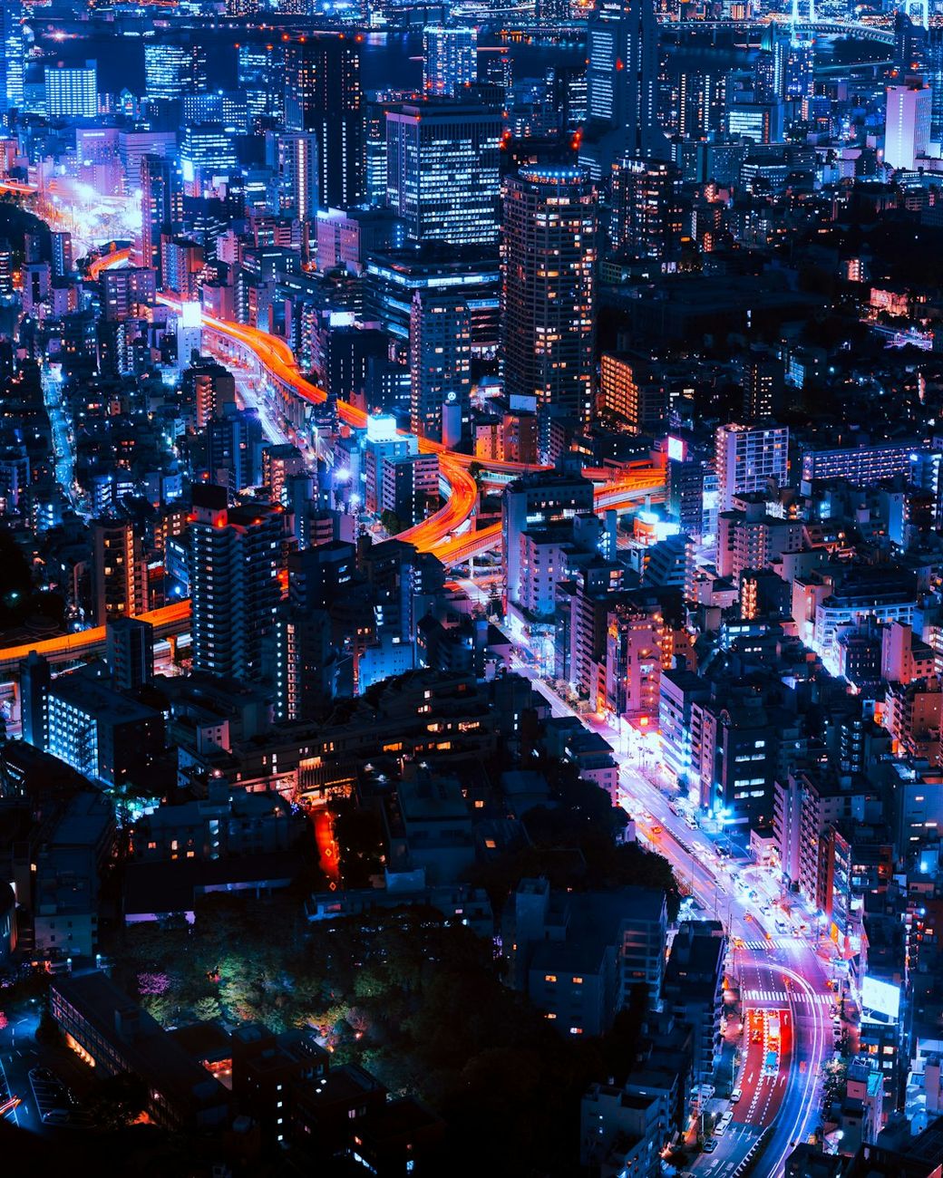 The image showcases a vibrant aerial view of a bustling cityscape at night, illuminated by a multitude of colorful lights. Skyscrapers and urban infrastructure are prominently featured, reflecting the dynamic energy of urban life. — Credit: Photo by Pawel Nolbert on Unsplash