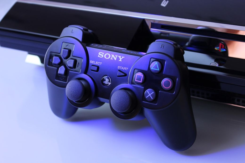 The image features a Sony PlayStation 3 console alongside its matching black controller. The controller is prominently displayed with clear visibility of its buttons and branding. — Credit: Photo by Nikita Kostrykin on Unsplash