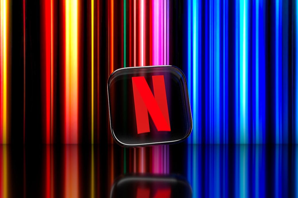 The image features the Netflix logo prominently displayed against a backdrop of colorful vertical light bars. The glossy surface reflects the logo, highlighting its vibrant colors. — Credit: Photo by Dima Solomin on Unsplash