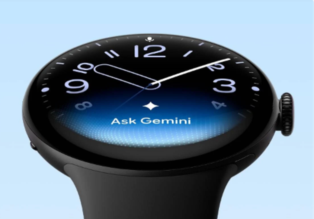 The image features a close-up of a smartwatch displaying a blue gradient background and a query for 'Ask Gemini' on its screen. The watch has a sleek design with prominent hour and minute hands.