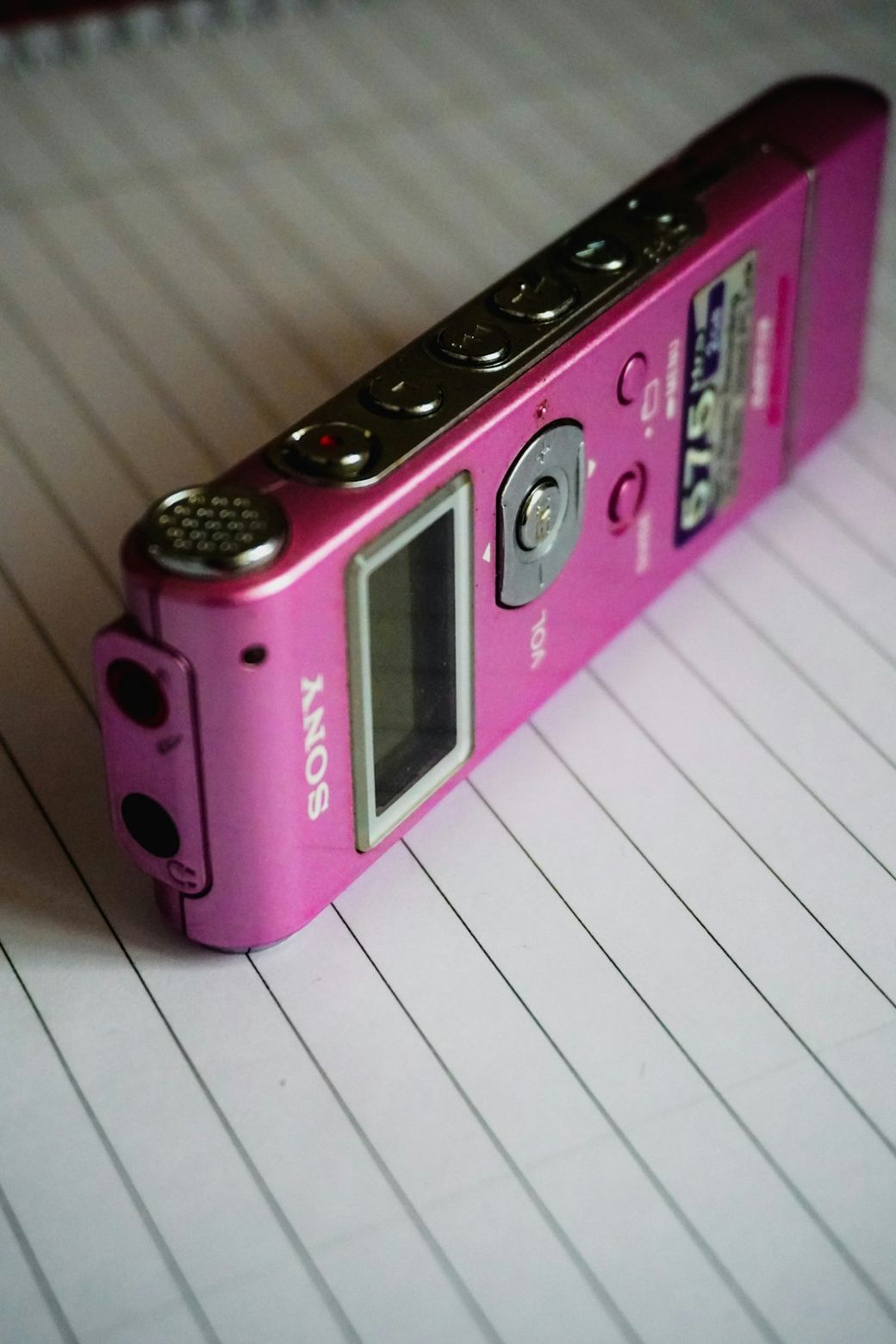 The image depicts a pink Sony voice recorder placed on lined notebook paper. The device features buttons on its side, indicating its functionality for recording audio. — Credit: Photo by Adhitya Sibikumar on Unsplash