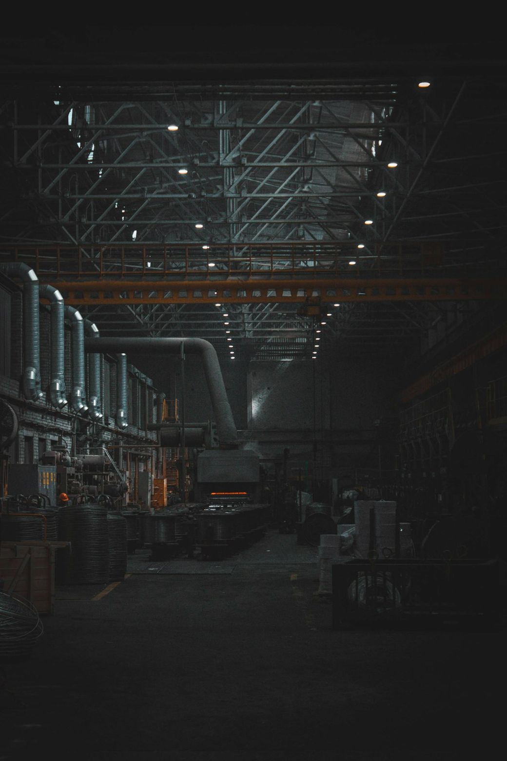 An industrial warehouse interior featuring a large, dimly lit space with high ceilings and structural beams. The scene includes machinery and production equipment, emphasizing the manufacturing aspect of the environment. — Credit: Photo by Shavr IK on Unsplash
