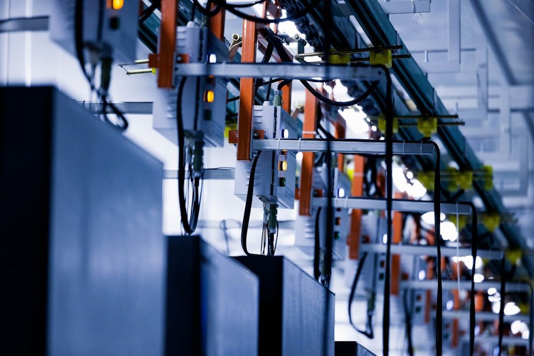 The image showcases a close-up view of machinery equipped with various components and cables, likely used in a manufacturing or industrial setting. The focused lighting and intricate design highlight the complexity of the equipment. — Credit: Photo by Homa Appliances on Unsplash