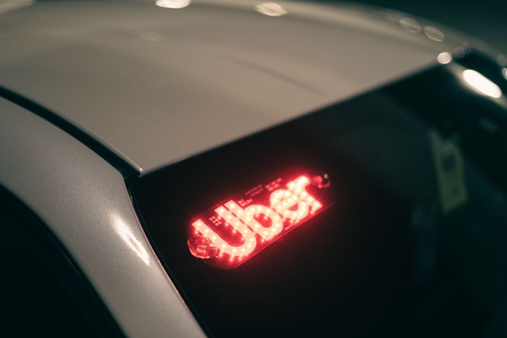 The image shows the rear of a vehicle with a glowing Uber sign, indicating the car is likely in use for ride-sharing services. The setting appears to be indoors, possibly a garage or a parking area. — Credit: Photo by Erik Mclean on Unsplash