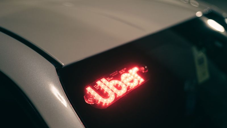 The image shows the rear of a vehicle with a glowing Uber sign, indicating the car is likely in use for ride-sharing services. The setting appears to be indoors, possibly a garage or a parking area.