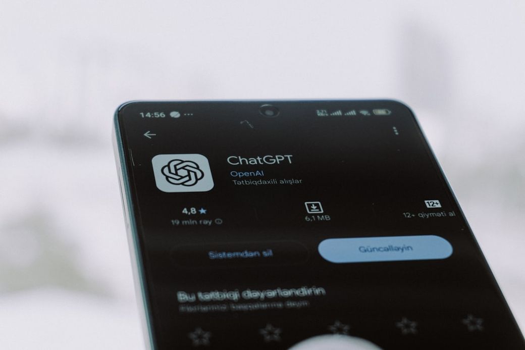 A close-up of a smartphone displaying the ChatGPT application interface, showcasing its rating and download details. The background is blurred with a cold, wintry atmosphere. — Credit: Photo by Zulfugar Karimov on Unsplash