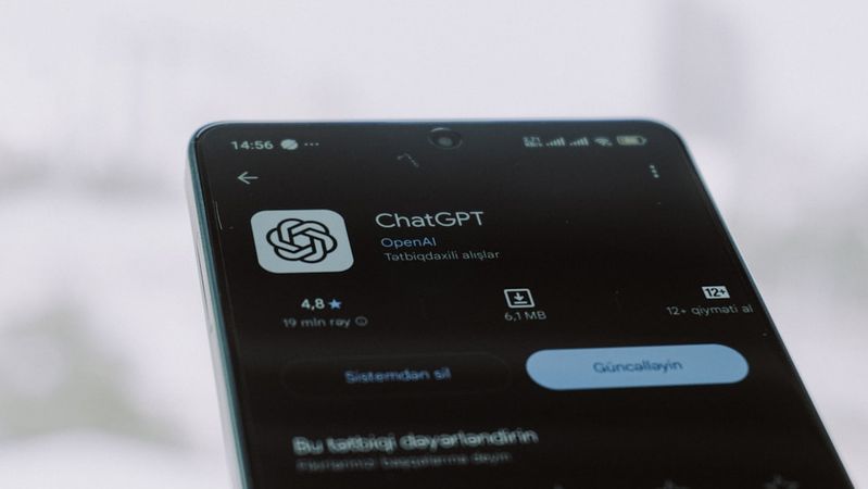 A close-up of a smartphone displaying the ChatGPT application interface, showcasing its rating and download details. The background is blurred with a cold, wintry atmosphere.