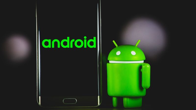 The image features a smartphone displaying the 'android' logo on its screen alongside a green Android figurine. The background is dark, emphasizing the bright colors of the logo and figurine.