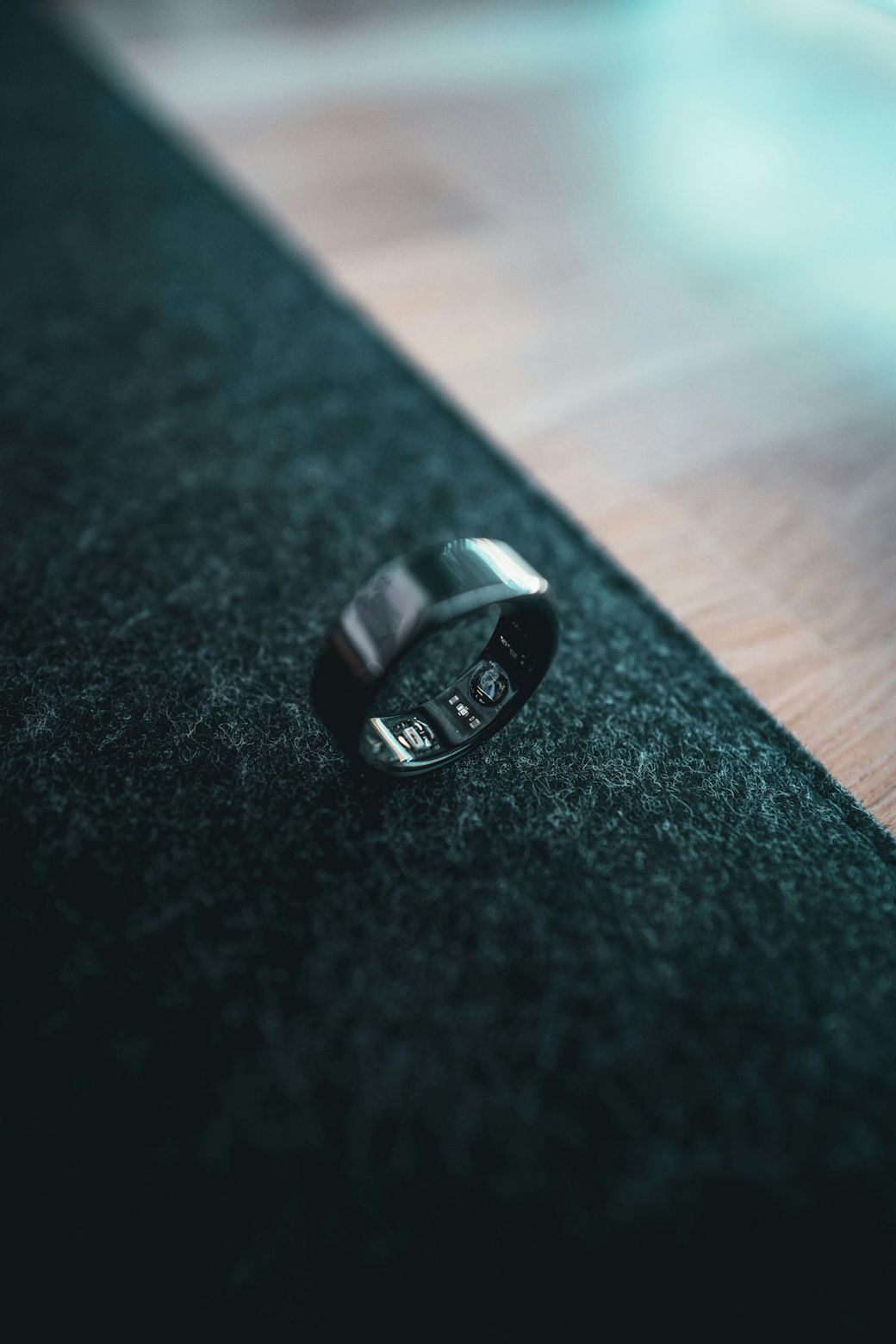 The image features a close-up of a sleek black ring placed on a textured dark surface, highlighting its polished design. The background shows hints of wood flooring, providing a contrast to the ring's dark color. — Credit: Photo by Jerry Kavan on Unsplash