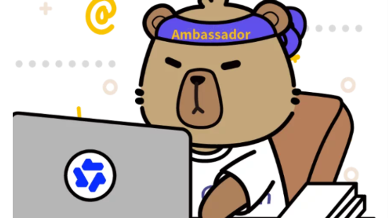 The image features a cartoon bear character wearing a headband labeled 'Ambassador' and typing at a desk with a computer. The bear appears focused as it engages in an online activity, indicating a role related to communication or representation in a digital context.