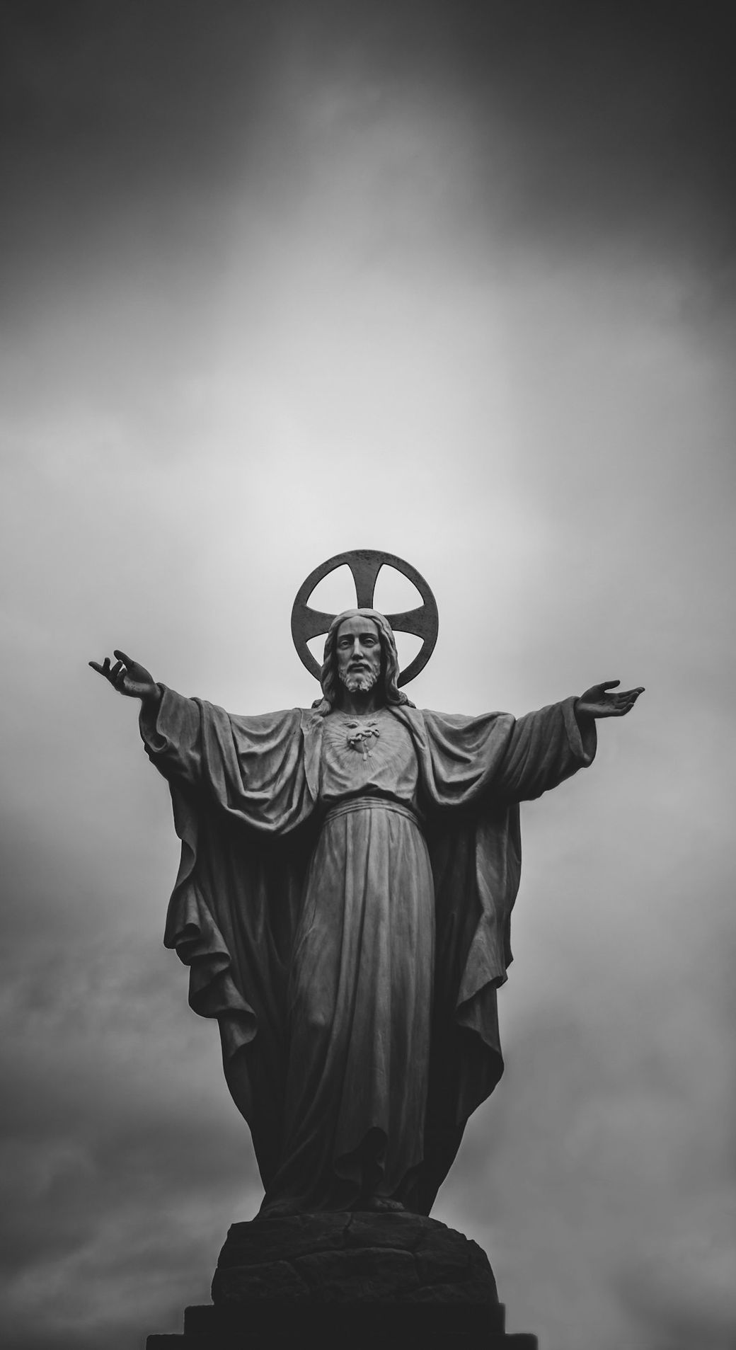 A black and white image of a large statue depicting Jesus Christ with outstretched arms. The statue is set against a cloudy sky, enhancing its dramatic presence. — Credit: Photo by Arturo Rey on Unsplash
