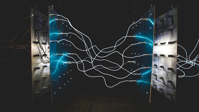 The image displays an abstract arrangement of metallic panels connected by glowing wires, creating a visually striking composition. The contrasting lights against a dark backdrop evoke a sense of technological innovation.
