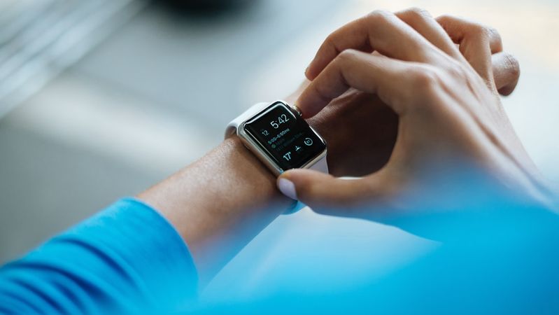 A close-up image of a person adjusting a smartwatch on their wrist. The device displays time and additional functionalities, highlighting its modern design and technology.