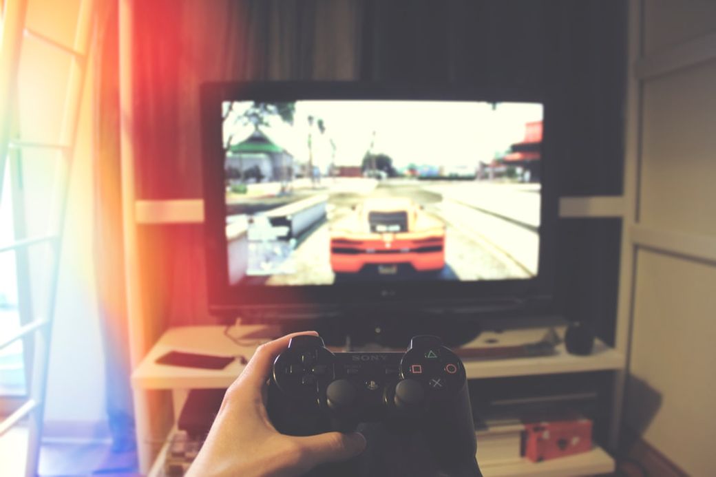 A person is holding a game controller while playing a video game on a television screen. The image captures a gaming setup in a cozy living room environment. — Credit: Photo by João Ferrão on Unsplash