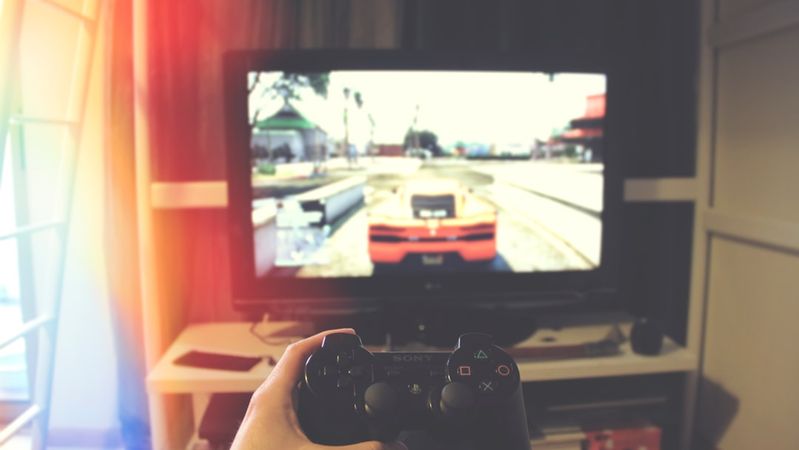 A person is holding a game controller while playing a video game on a television screen. The image captures a gaming setup in a cozy living room environment.