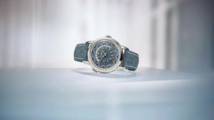 A Patek Philippe World Time watch with a blue-gray dial and denim-blue strap on a white surface