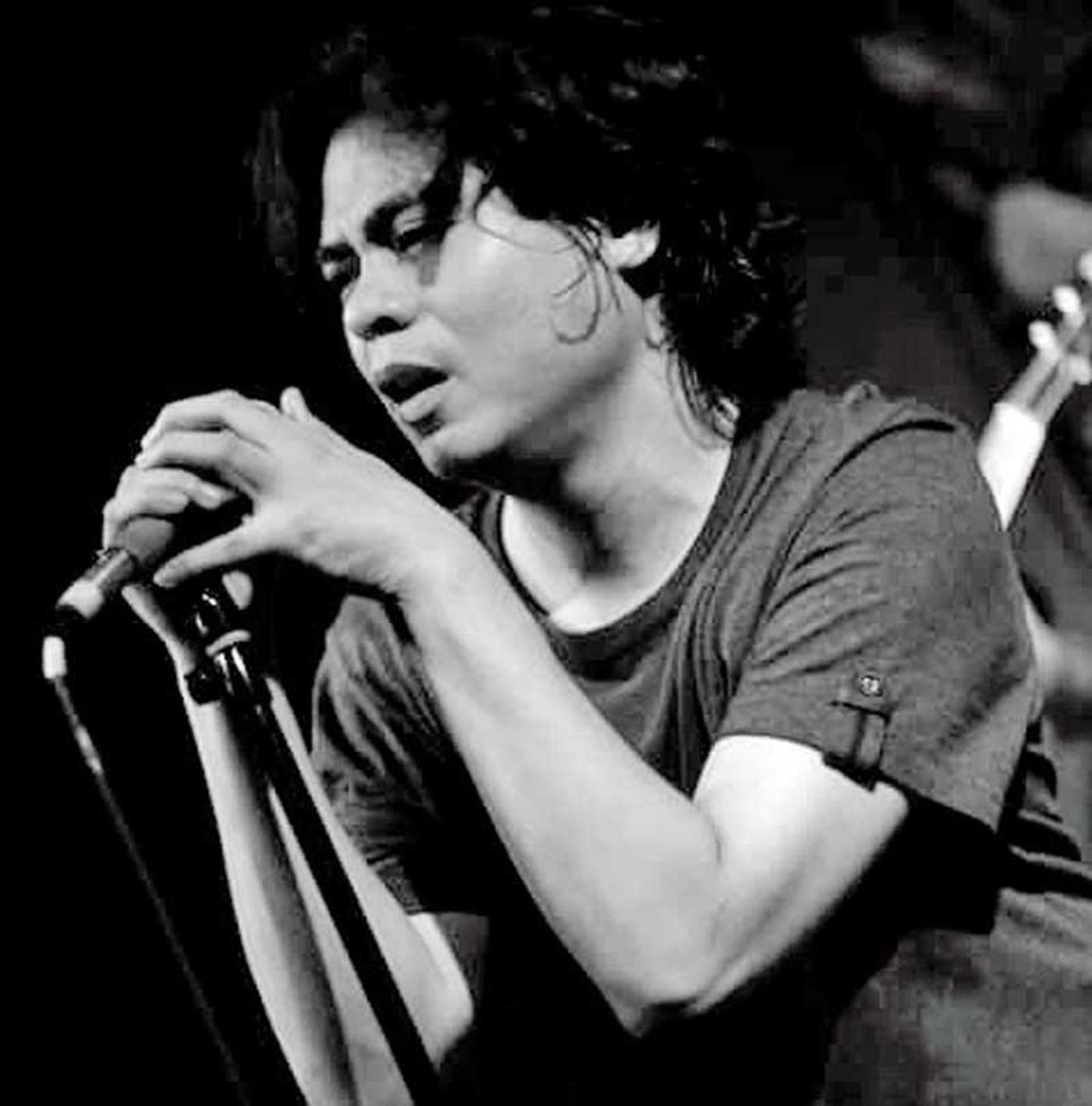 Kevin Roy leaning into a microphone mid-song, hair falling across his face, in black and white