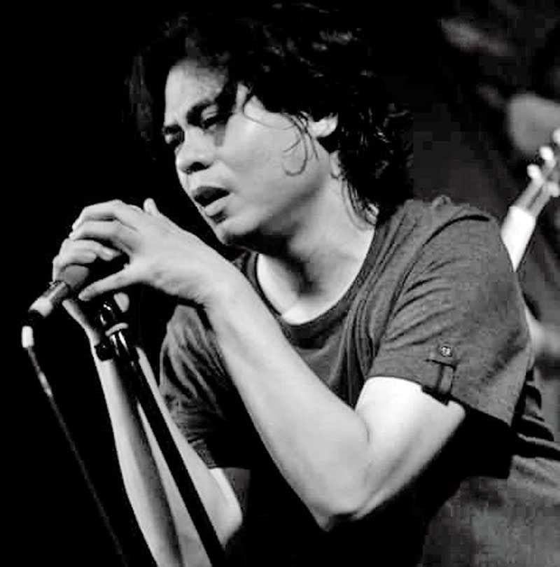 Kevin Roy leaning into a microphone mid-song, hair falling across his face, in black and white