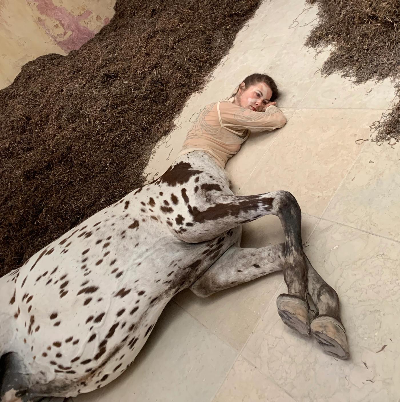 Detail of a lifelike dead female centaur with a spotted horse body lying on pale stone tiles