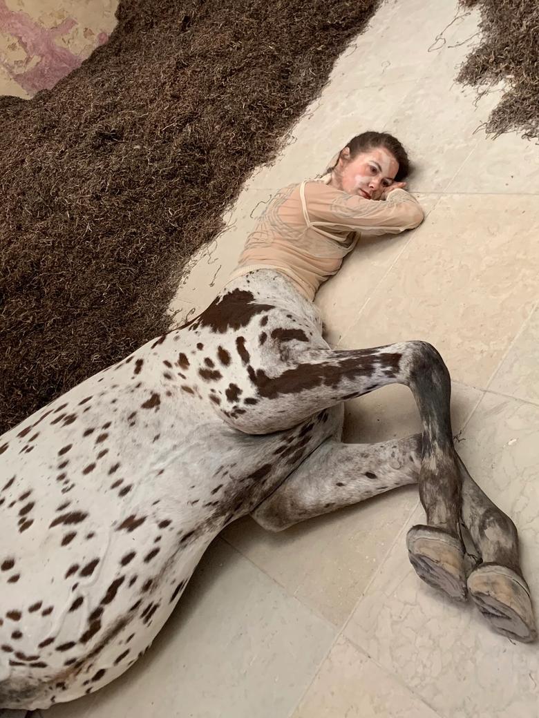 Detail of a lifelike dead female centaur with a spotted horse body lying on pale stone tiles