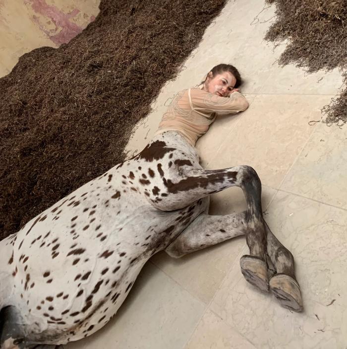 Detail of a lifelike dead female centaur with a spotted horse body lying on pale stone tiles