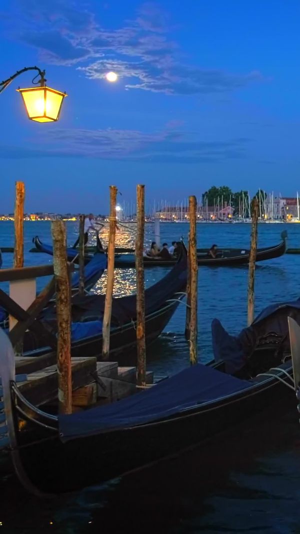 Gondolas moored in the Venice lagoon at blue hour under a full moon