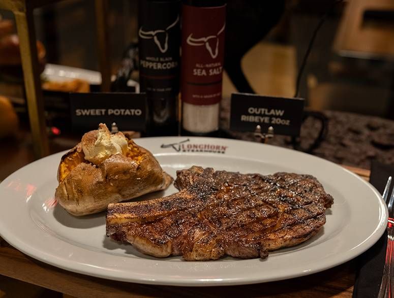 Charred Outlaw Ribeye with a butter-topped baked potato, seasoning bottles lined up behind