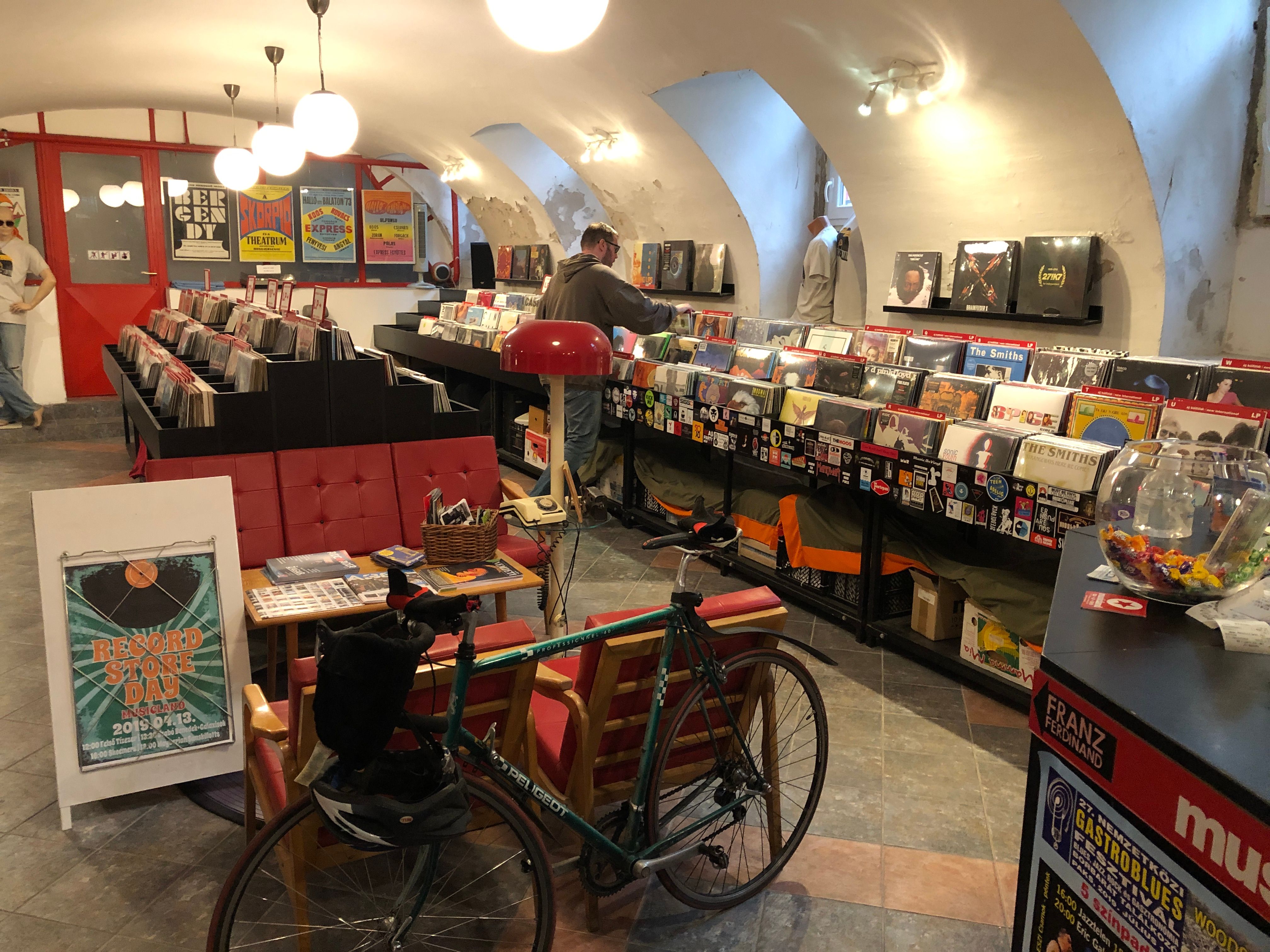 Shopper browsing record bins in a vaulted cellar store with red benches and a parked bicycle