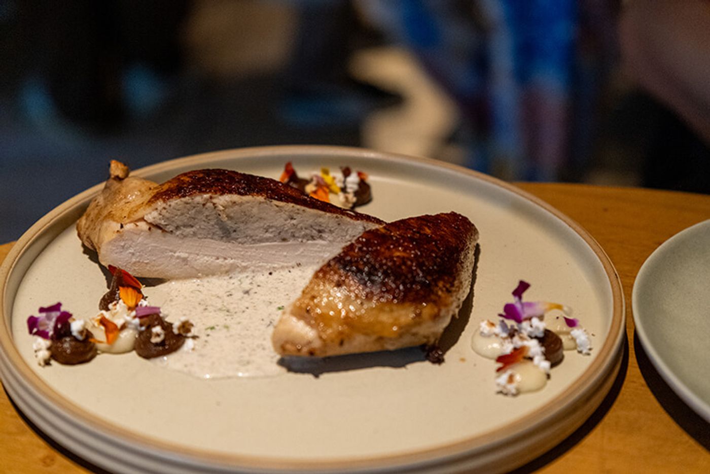 Roasted truffle-stuffed chicken breast sliced open on a plate with caramelized onion puree and petals