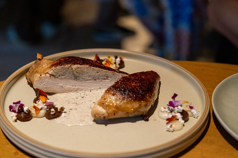 Roasted truffle-stuffed chicken breast sliced open on a plate with caramelized onion puree and petals