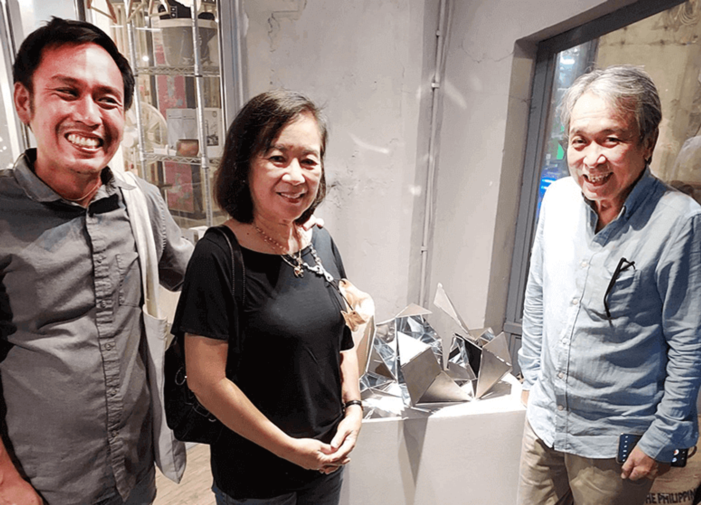 Conceptual artist Marco Ortiga, Nancy Ortiga and Sari Ortiga smiling beside a mirrored sculpture