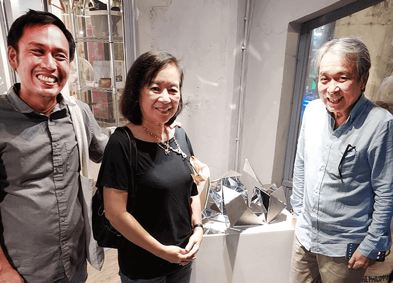Conceptual artist Marco Ortiga, Nancy Ortiga and Sari Ortiga smiling beside a mirrored sculpture