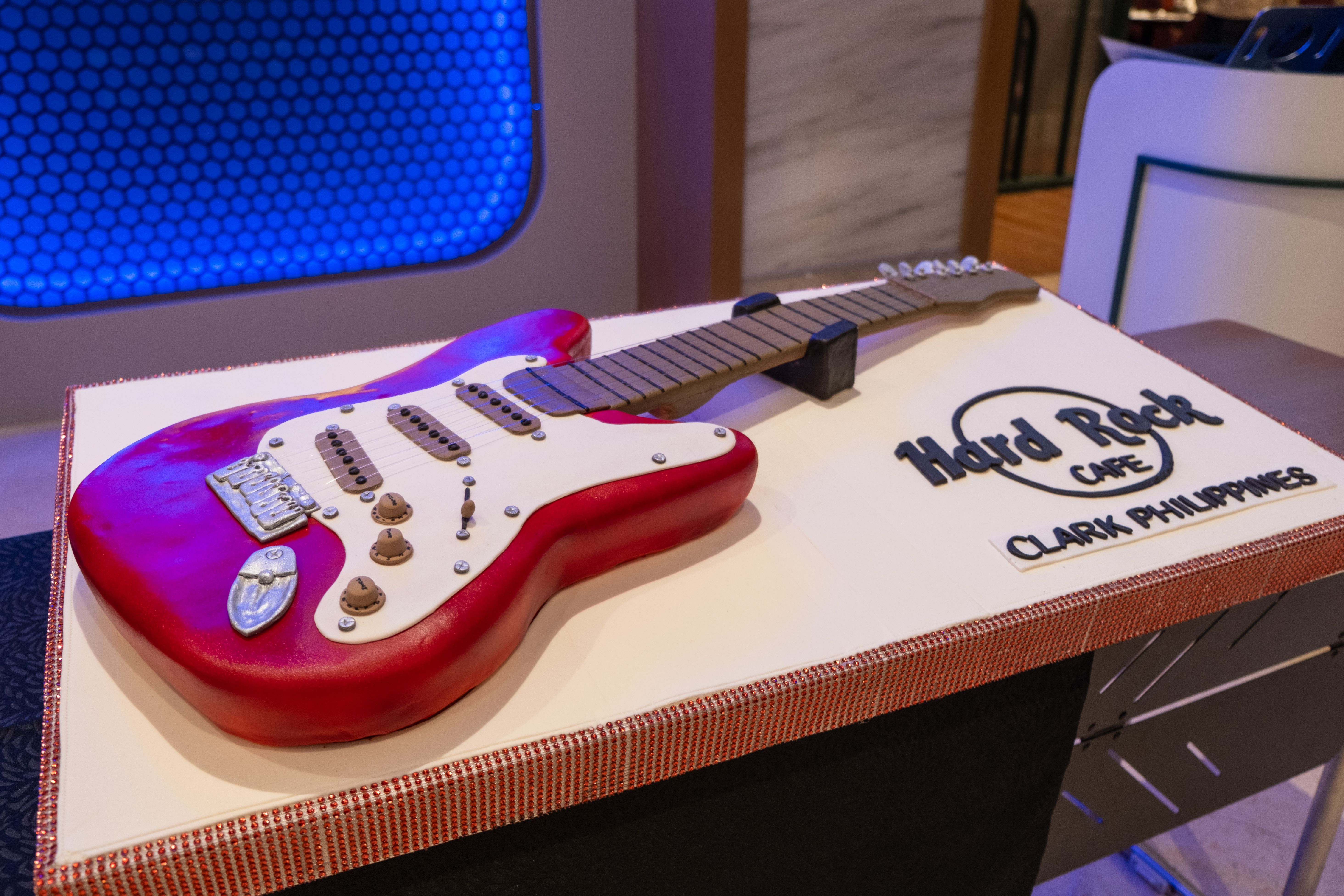 Cake shaped like a red electric guitar beside the Hard Rock Cafe Clark Philippines logo