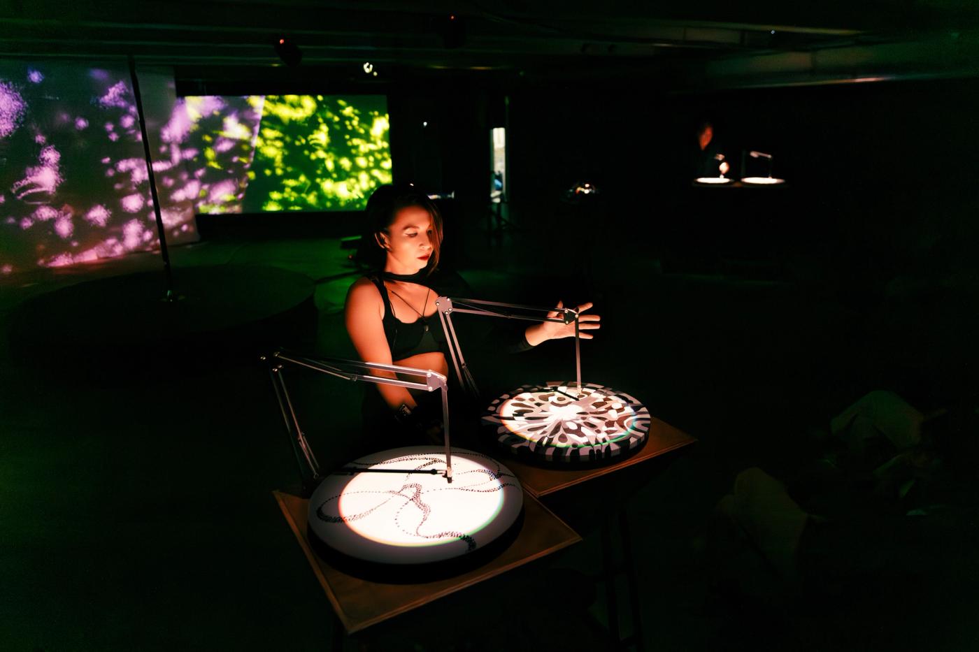 Christina Dy smiling on stage as she operates the Plaka Reader audio-kinetic machine under blue lights