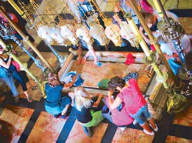 Pilgrims kneel to touch the Stone of Anointing beneath a row of hanging lamps