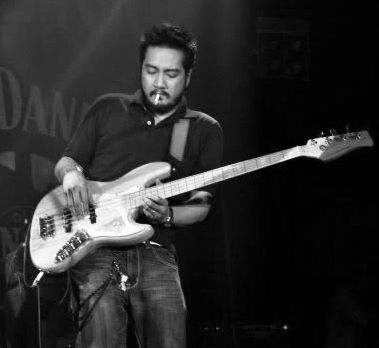 Louie Talan playing bass onstage with a cigarette between his lips, in black and white