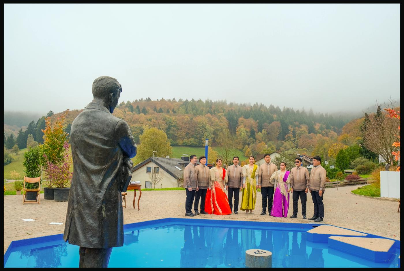 The Philippine Madrigal Singers in formal wear face the Rizal statue across a blue tiled fountain