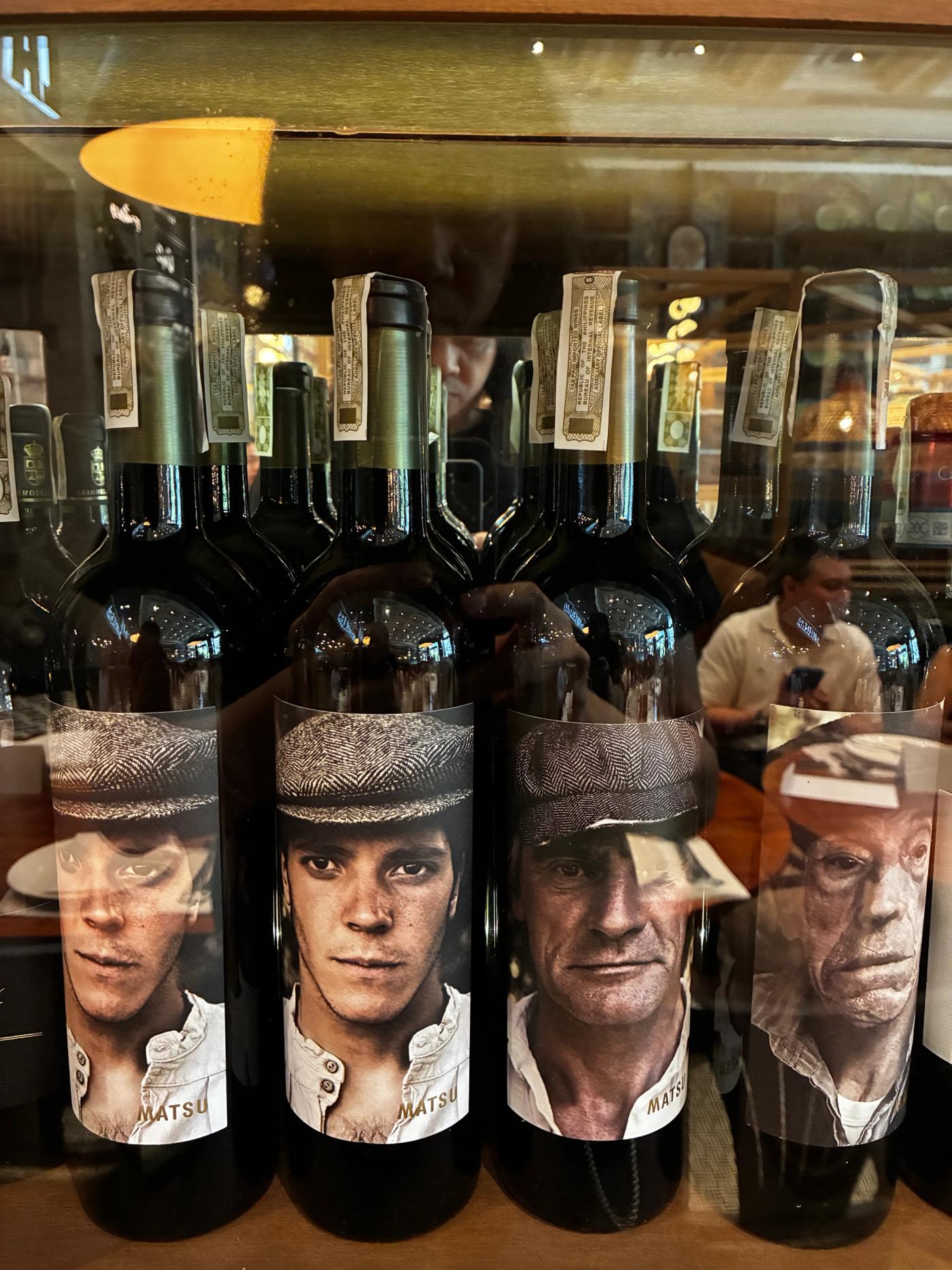 Matsu wine bottles in a display case, each label bearing the portrait of a flat-capped farmer