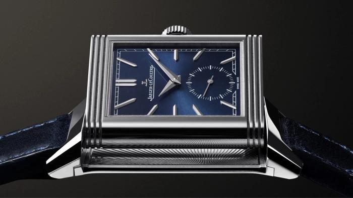 Steel Jaeger-LeCoultre Reverso with a sunray blue dial and small-seconds counter, its rectangular case caught mid-swivel above a navy leather strap, against black