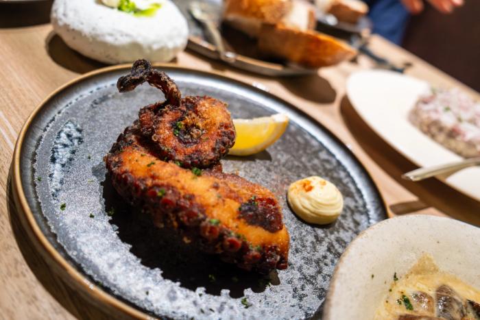 A curled fried octopus tentacle with a lemon wedge and a dollop of aioli on a dark ceramic plate at Juniper in Ortigas